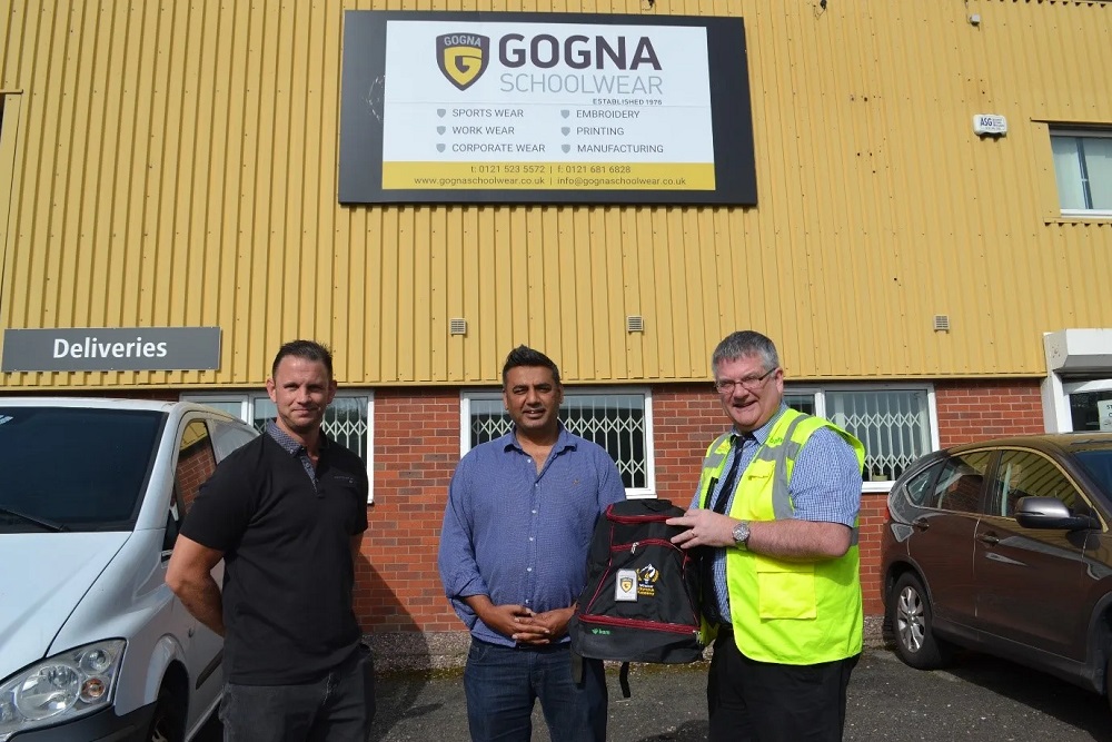 Photo of three people, one of which is holding one of the donated bags to the school